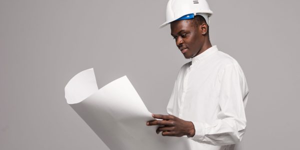 Portrait of confident, smiling afro american architect man with blueprint, looking at camera on gray background